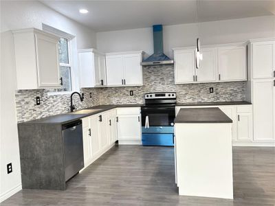 Kitchen with sink, stainless steel appliances, wall chimney range hood, decorative light fixtures, and a kitchen island.