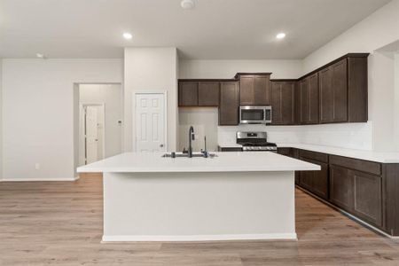 This light and bright kitchen features a large quartz island, dark stained cabinets, a large sink overlooking your family room, recessed lighting, and beautiful backsplash.