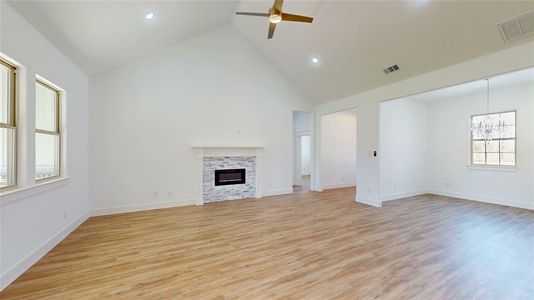 Unfurnished living room featuring ceiling fan with notable chandelier, light wood-style flooring, a fireplace, and visible vents