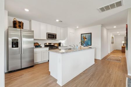 Kitchen with white cabinets, stainless steel appliances, a center island with sink, and light wood-type flooring