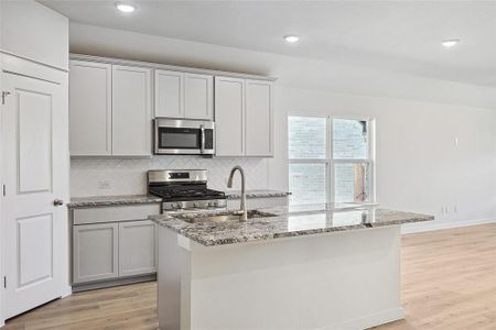 Kitchen featuring backsplash, light wood-type flooring, stainless steel appliances, sink, and a center island with sink