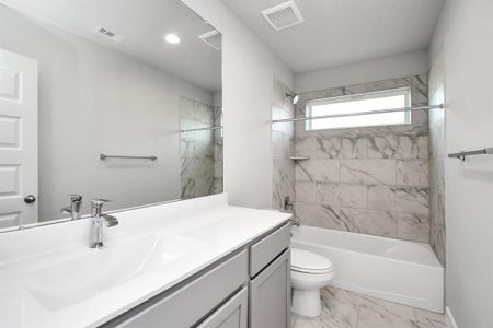 The secondary bath includes modern tile flooring, a combined bath and shower with a tile surround, light wood cabinetry, and a beautiful light-colored countertop. Sample photo of similar plan. Actual colors and selections may vary.