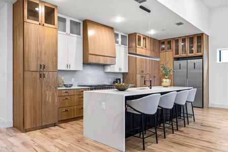 Kitchen featuring light wood-type flooring, stainless steel appliances, white cabinetry, and an island with sink