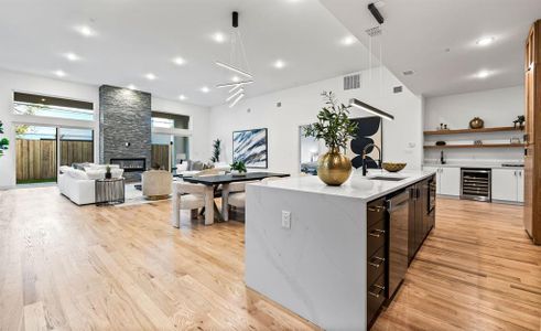 Kitchen with sink, wine cooler, a fireplace, light stone countertops, and a center island with sink