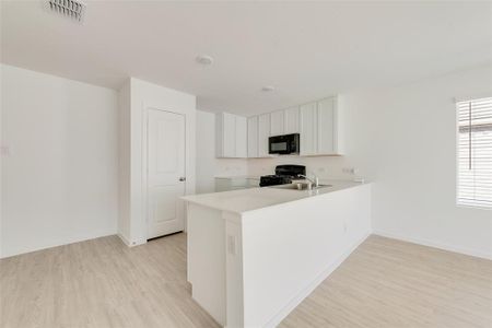 Kitchen with light wood-type flooring, kitchen peninsula, black appliances, sink, and white cabinets