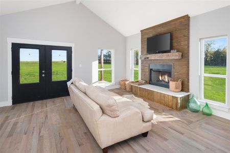 Living room with high vaulted ceiling, french doors, light hardwood / wood-style floors, beamed ceiling, and a large fireplace