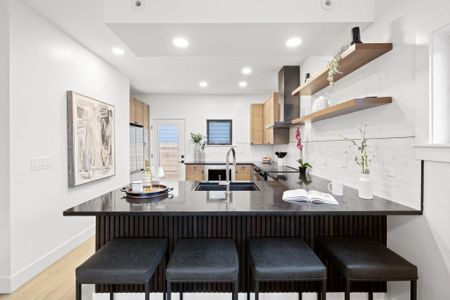 Kitchen with light wood finished floors, a peninsula, a sink, decorative backsplash, and wall chimney range hood