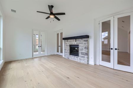 Unfurnished living room featuring french doors, light hardwood / wood-style flooring, a stone fireplace, and ceiling fan