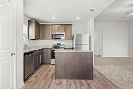 Kitchen featuring stainless steel appliances, a sink, light stone counters, a center island, and light wood-style floors Kitchen featuring stainless steel appliances, a sink, light stone counters, a center island, and light wood-style floors