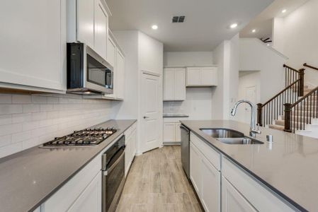 Kitchen with backsplash, stainless steel appliances, sink, white cabinets, and light hardwood / wood-style floors