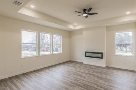 Unfurnished living room with a raised ceiling, light hardwood / wood-style floors, and ceiling fan