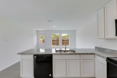 Kitchen featuring white cabinetry, light tile patterned floors, light stone counters, black dishwasher, and sink