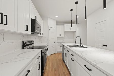 Kitchen featuring sink, pendant lighting, stainless steel appliances, light stone countertops, and white cabinets