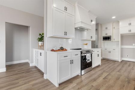 Kitchen featuring white cabinetry, light hardwood / wood-style flooring, stainless steel appliances, and custom exhaust hood