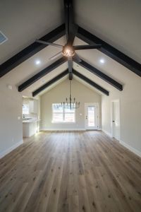 Unfurnished living room with wood finished floors, visible vents, baseboards, lofted ceiling with beams, and ceiling fan