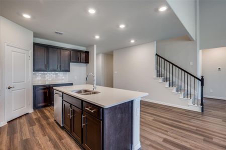 Kitchen with sink, dark hardwood / wood-style flooring, tasteful backsplash, and a kitchen island with sink