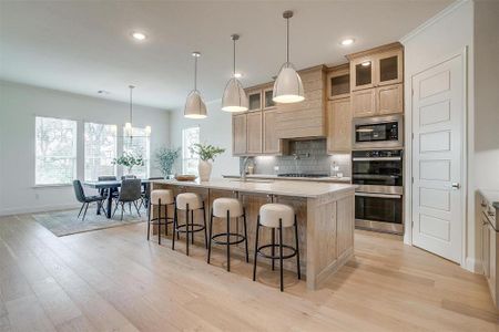 Kitchen featuring light hardwood flooring, a kitchen island with leathered Quartzite countertops, farm sink, natural stain custom cabinetry with soft close drawers and cabinets.