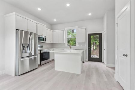 Kitchen with light wood-type flooring, a center island, sink, white cabinets, and stainless steel appliances