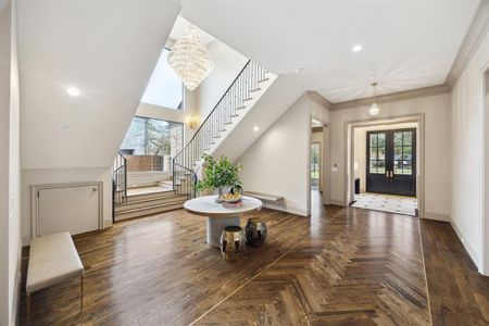 This uniquely captivating entryway features a sweeping staircase with sleek iron railings, a dazzling crystal chandelier, and oversized windows that bathe the space in light. The herringbone hardwood floors, detailed millwork, and a striking round table make this an unforgettable and inviting first impression.