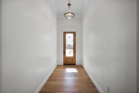 Doorway to outside with ornamental molding, a notable chandelier, and light wood-type flooring