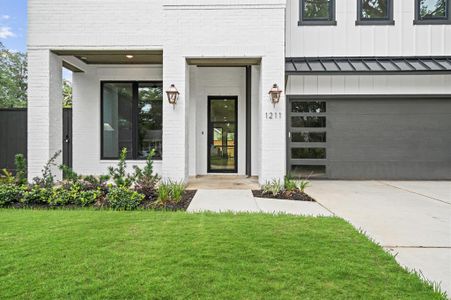 Covered front porch welcoming guests, flanked by large windows and warm lanterns, set against a neatly landscaped yard.