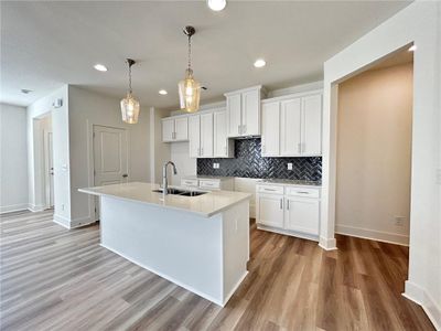 Kitchen with sink, a kitchen island with sink, hanging light fixtures, light hardwood / wood-style floors, and white cabinets