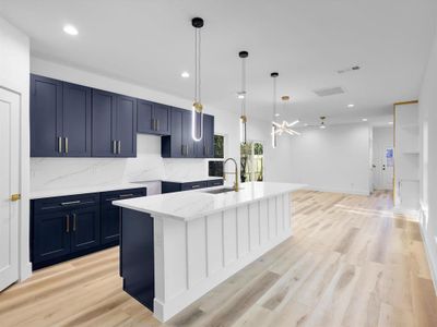 Kitchen featuring decorative backsplash, a kitchen island with sink, sink, decorative light fixtures, and light hardwood / wood-style floors