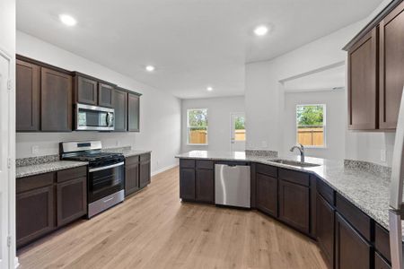 Kitchen with dark brown cabinets, stainless steel appliances, sink, light stone countertops, and light hardwood / wood-style floors