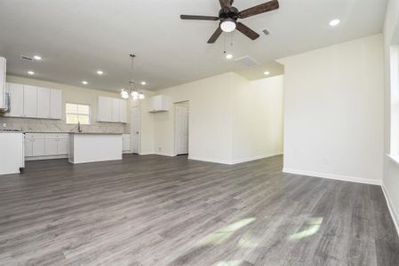 Spacious, empty room with gray flooring, white kitchen cabinetry, modern lighting, and neutral walls; appears to be a new or renovated home.