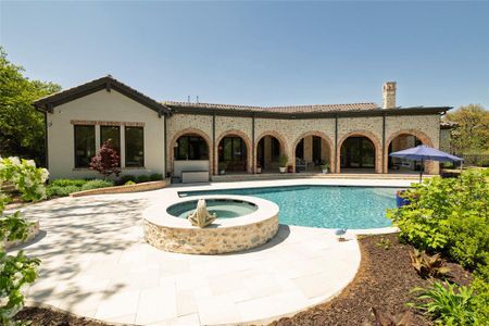 Back of property featuring brick siding, a pool with connected hot tub, a patio, and a chimney