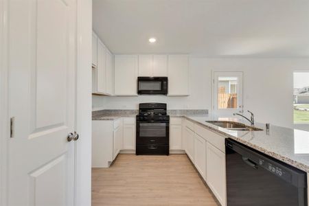 Kitchen with light hardwood / wood-style floors, white cabinetry, sink, light stone counters, and black appliances