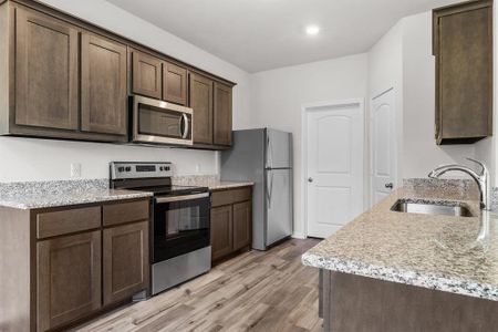 Kitchen featuring sink, light hardwood / wood-style flooring, appliances with stainless steel finishes, dark brown cabinets, and light stone counters