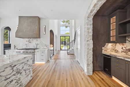 View of the wet bar (complete with separate ice maker and beverage cooler) with lime wash paint, custom cabient hardware, and marble counters on the right, conveniently located across from the kitchen with waterfall edge island.