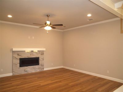 Unfurnished living room featuring hardwood / wood-style floors, crown molding, a fireplace, and ceiling fan