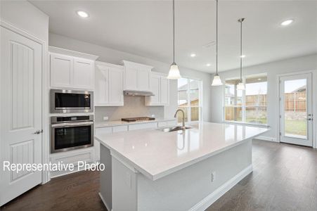 Kitchen with dark hardwood / wood-style floors, appliances with stainless steel finishes, sink, decorative backsplash, and a center island with sink