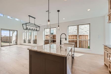 Kitchen with light stone countertops, a wealth of natural light, a center island with sink, and light hardwood / wood-style flooring