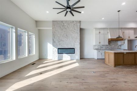 Kitchen and living featuring 12 foot ceilings, stone fireplace, white cabinets and stained island, decorative light fixtures, and engineered wood flooring. This Home is under construction and not the property for sale but representative of finish out of Residence #110