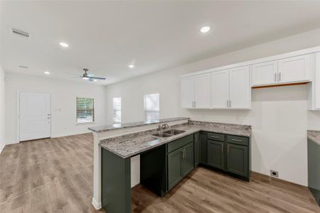 Kitchen with green cabinets, ceiling fan, white cabinets, light stone counters, and light hardwood / wood-style flooring