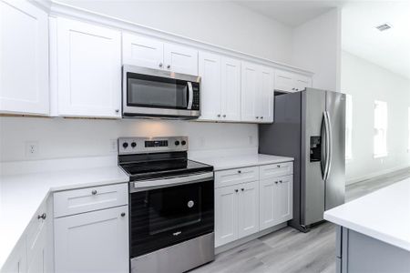 Kitchen with stainless steel appliances, light hardwood / wood-style floors, and white cabinets