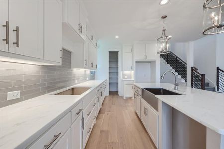 Kitchen featuring hanging light fixtures, tasteful backsplash, white cabinetry, light stone countertops, and light wood-type flooring