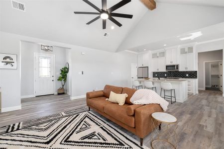 Living room with high vaulted ceiling, ceiling fan with notable chandelier, light hardwood / wood-style floors, and beamed ceiling