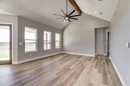 Unfurnished living room featuring light wood-type flooring, ceiling fan, beamed ceiling, and high vaulted ceiling