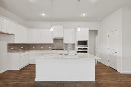 Kitchen with sink, an island with sink, hanging light fixtures, and white cabinetry