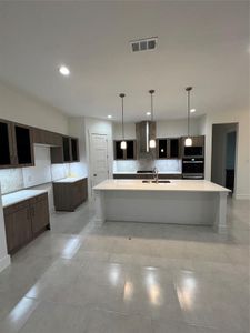 Kitchen featuring backsplash, dark brown cabinets, sink, exhaust hood, and a center island with sink