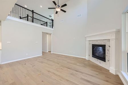 Unfurnished living room featuring a towering ceiling, a premium fireplace, and light hardwood / wood-style floors