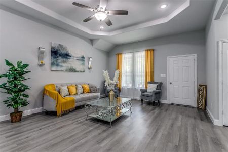 Living room with a raised ceiling, ceiling fan, and light hardwood / wood-style floors