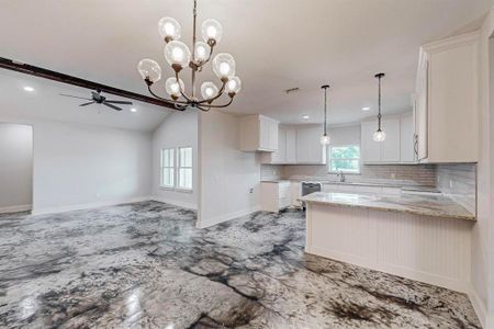 Kitchen featuring decorative backsplash, light stone countertops, ceiling fan with notable chandelier, white cabinets, and vaulted ceiling with beams