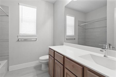 Secondary bath features tile flooring, bath/shower combo with tile surround, stained wood cabinets, beautiful light countertops, mirror, sleek fixtures and modern finishes.