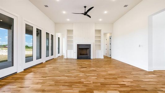 Unfurnished living room with built in features, ceiling fan, a large fireplace, and light wood-type flooring