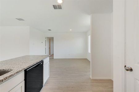 Kitchen featuring light wood-type flooring, black dishwasher, light stone counters, and white cabinets